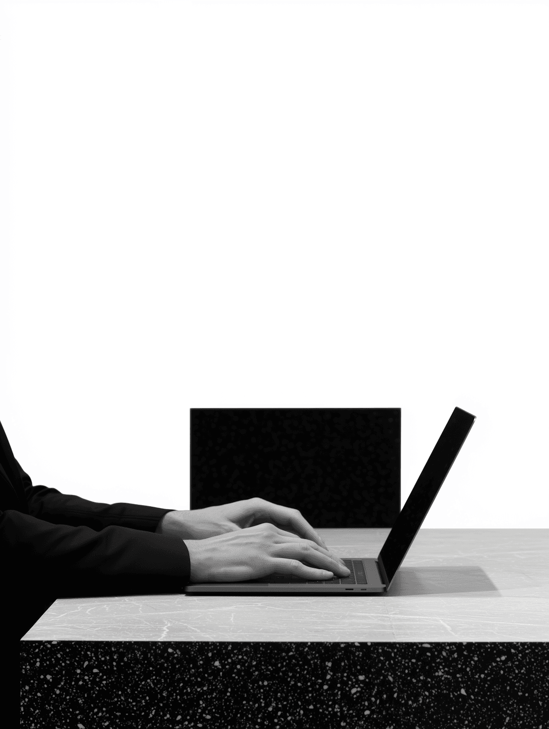 Hands typing on a laptop at a minimal desk in black and white